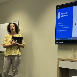 Gemma standing next to a screen, doing a presentation. 